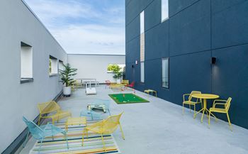 a patio with yellow and blue chairs and tables and a green rug